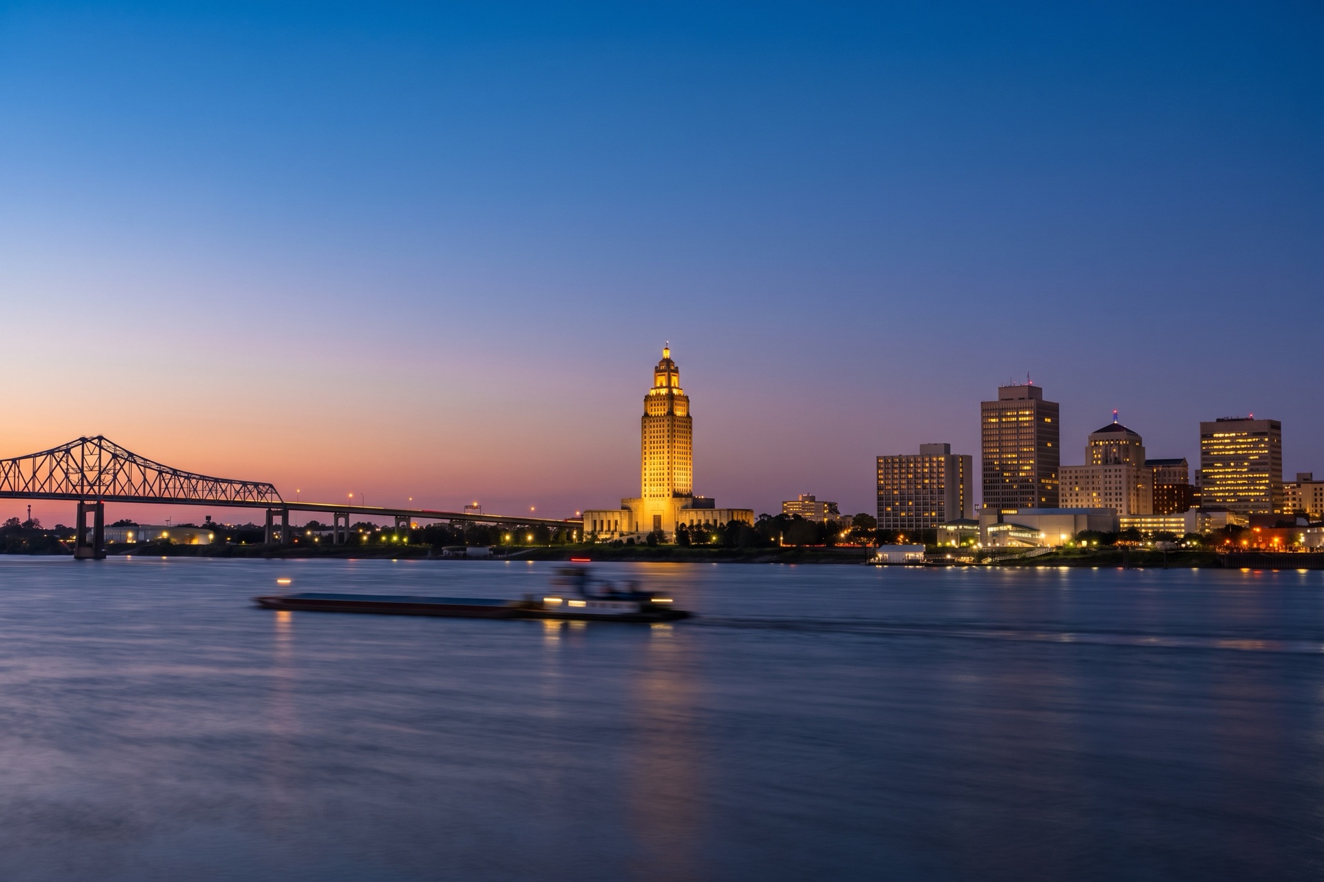 Downtown Baton Rouge skyline at dusk with the Louisiana State Capitol tower and the Mississippi River bridge